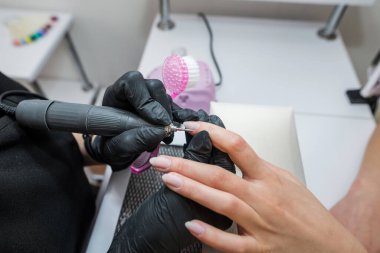 Bir manikürcü, bir güzellik salonunun müşterisine manikür yapar. Tırnak makasının yakın plan çıkarılması. Üstat tırnak derisini budamak ve sökmek için elektrikli tırnak dosyası kullanıyor.