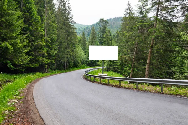 Empty white horizontal billboard on the roadside. A curved road between the forest.