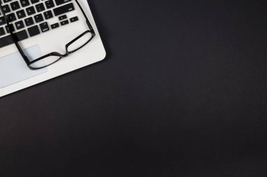 Siyah zemin üzerinde gözlük bulunan ve kopyalama alanı olan bir klavyenin üst görünümü.