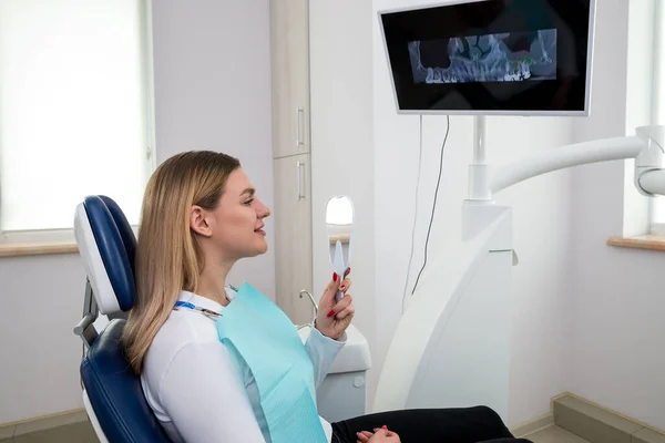 Close-up of a girl looking in the mirror at her white teeth while sitting in a chair at the dentist.