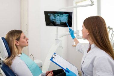 Diş hekimi, hastanın çenesinin röntgenini gösteriyor. Dişçi kliniğindeki danışmanlık sırasında doktor ve kadın müşteri. Tartışılan konular. Tıbbi sağlık ve stomatolojik yardım. Profesyonel atama