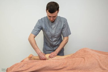 Bir erkek masaj terapisti masaj masasında yatan genç bir kadının bacağına masaj yapıyor..