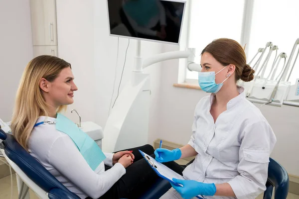 The woman went to the dentist. She is sitting in the dentist\'s chair. The dentist explains and advises the patient.a female dentist in a dental office is talking to a patient and preparing for treatment.