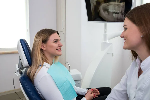 The woman went to the dentist. She is sitting in the dentist\'s chair. The dentist explains and advises the patient.a female dentist in a dental office is talking to a patient and preparing for treatment.