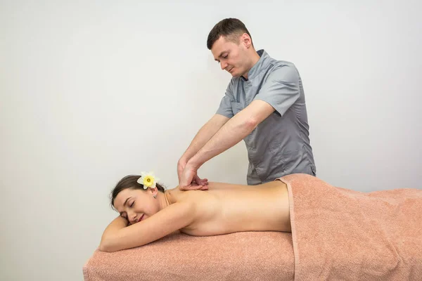 Back massage in a massage parlor. A male massage therapist makes a back and body massage to a young beautiful brunette woman.