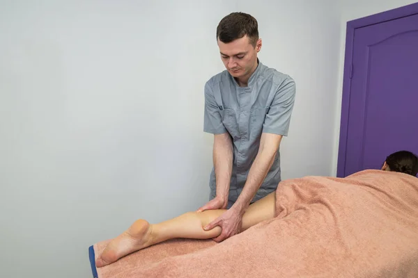 Egy Férfi Masszázsterapeuta Masszírozza Egy Masszázsasztalon Fekvő Fiatal Lábszárát — Stock Fotó