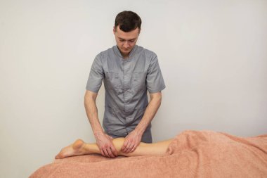 Bir erkek masaj terapisti masaj masasında yatan genç bir kadının bacağına masaj yapıyor..