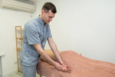 Bilek masajı. Bir erkek masaj terapisti masaj masasında yatan genç bir kadının bileğine masaj yapıyor..