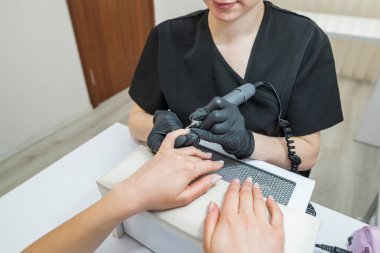 Manikürcüdeki elektrikli makinede profesyonel donanım manikürü. Tırnak derisini kesiciyle kaldırma işlemi. Usta tırnak etlerini budamak ve sökmek için elektrikli tırnak törpüsü kullanıyor.