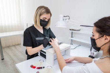 Manikür ustası bir manikürcüde eski tırnak cilasını sökmek için elektrikli oje kullanıyor..