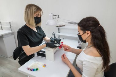 Tırnak rengi seçimi. Genç bir kız bir güzellik salonunda tırnaklarının rengini seçer. Tırnakların güzelliği ve sağlığı. Manikür ve manikür salonu müşterisi