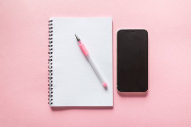 İzole edilmiş pembe arkaplan üzerinde kalem ve akıllı telefona sahip beyaz not defteri.