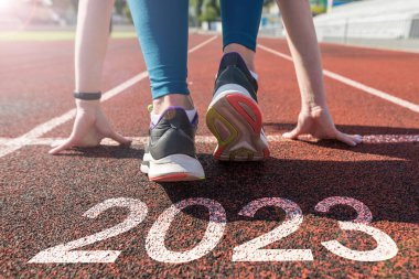 Rear view of a woman preparing to start on an athletics track engraved with the year 2023