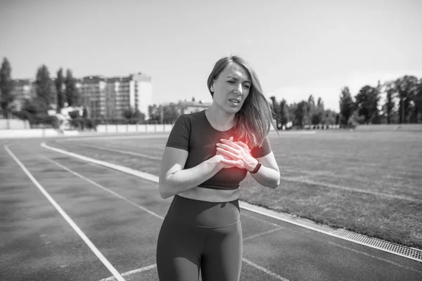 Black and white photo. Injury and pain in the chest of a female runner. A woman suffers from chest pains or symptoms of heart disease while running on a treadmill in a sports stadium.