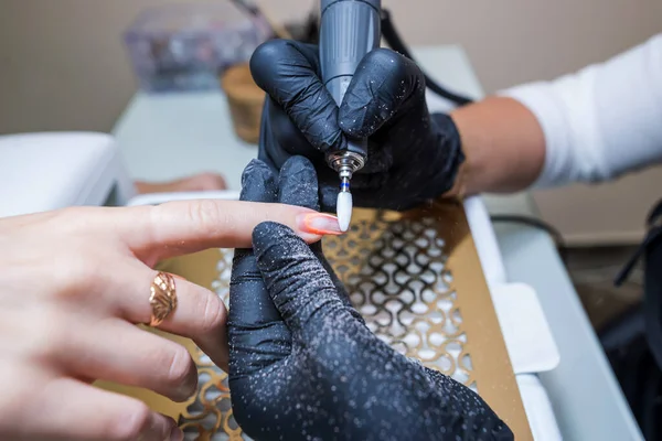 Close-up of a woman in a nail salon getting a manicure in a beauty salon from a beautician who uses an electric nail polish remover machine with flying shards all around. The concept of technology, nail care.