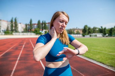 Fitness and healthy lifestyle. The trainer takes a break between exercises. Uses a smart watch to measure the pulse on the neck. A woman goes in for sports on a treadmill.