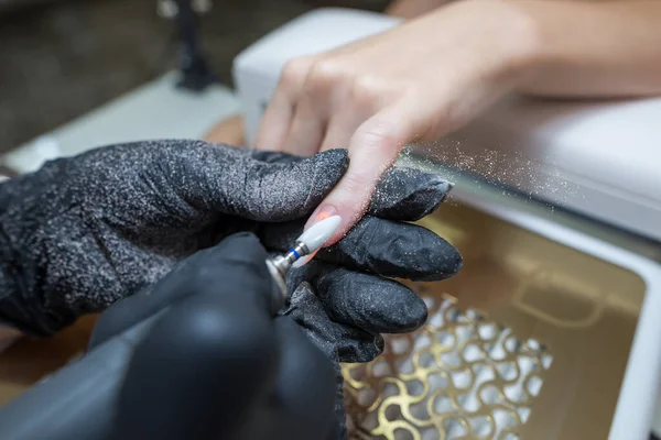 Close-up of a woman in a nail salon getting a manicure in a beauty salon from a beautician who uses an electric nail polish remover machine with flying shards all around. The concept of technology, nail care.