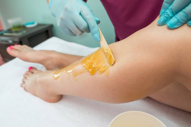 Woman undergoing leg hair removal procedure with sugaring paste in salon. Skin care, remove hair with sugar paste