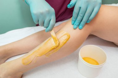 Woman undergoing leg hair removal procedure with sugaring paste in salon. Skin care, remove hair with sugar paste
