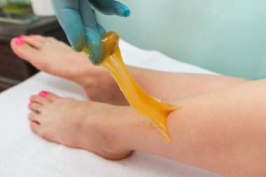 Woman undergoing leg hair removal procedure with sugaring paste in salon. Skin care, remove hair with sugar paste