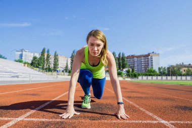 Spor pistinde koşmak için başlangıç pozisyonunda genç bir kadın. Başlangıçta sporcu kadın.