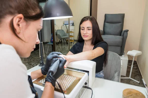 a woman in a nail salon gets a manicure in a beauty salon from a beautician who uses an electric nail polish remover machine. Nail care concept.