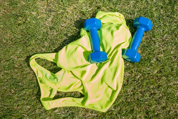 Top view of a sports jersey with dumbbells  on the grass of a football field.