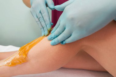 Woman undergoing leg hair removal procedure with sugaring paste in salon. Skin care, remove hair with sugar paste