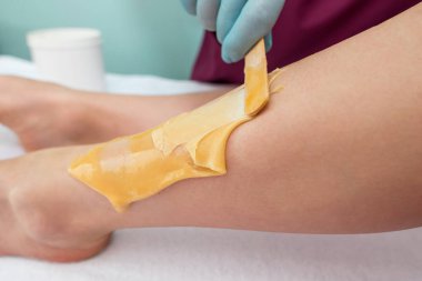 leg sugaring. A beautician makes a sugar paste depilation of a woman's legs in a beauty salon. Female aesthetic cosmetology. Apply sugar paste with a wooden spatula.
