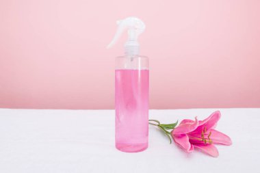Spray bottle with pink liquid and rose flower with copy space. The concept of cosmetology.