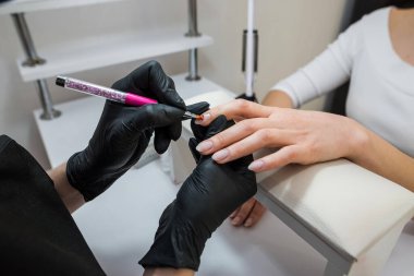 The manicurist applies a base layer to the client's nail.Applying a transparent varnish with a brush.The alignment of the nail plate with nail Polish.Professional  manicure in a beauty salon.