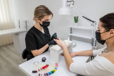 The manicurist applies a base layer to the client's nail.Applying a transparent varnish with a brush.The alignment of the nail plate with nail Polish.Professional  manicure in a beauty salon.