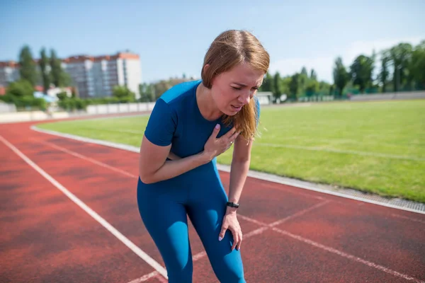 Injury and pain in the chest of a female runner. A woman suffers from chest pains or symptoms of heart disease while running on a treadmill in a sports stadium.
