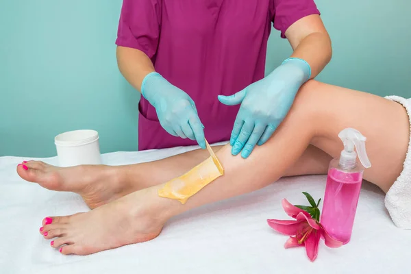 leg sugaring. A beautician makes a sugar paste depilation of a woman\'s legs in a beauty salon. Female aesthetic cosmetology. Apply sugar paste with a wooden spatula.