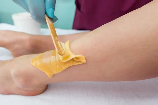 leg sugaring. A beautician makes a sugar paste depilation of a woman's legs in a beauty salon. Female aesthetic cosmetology. Apply sugar paste with a wooden spatula.