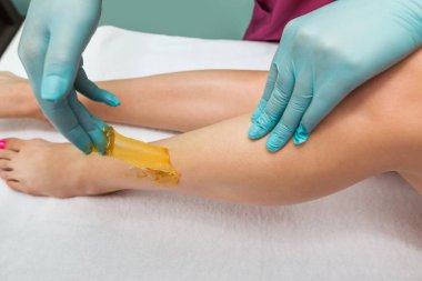 Woman undergoing leg hair removal procedure with sugaring paste in salon. Skin care, remove hair with sugar paste