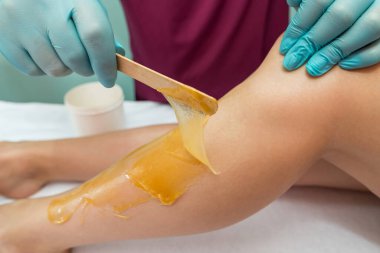 Woman undergoing leg hair removal procedure with sugaring paste in salon. Skin care, remove hair with sugar paste