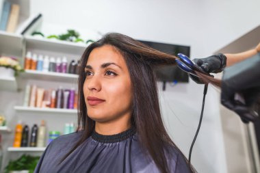 Hairdresser using a hair straightened to straighten the hair. Hair stylist working on a woman's hair style at salon.Hair care. Beautiful, attractive woman in a beauty salon.