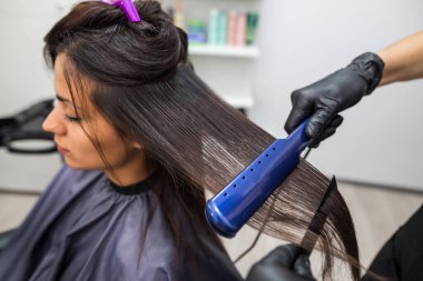 Hairdresser using a hair straightened to straighten the hair. Hair stylist working on a woman's hair style at salon.Hair care. Beautiful, attractive woman in a beauty salon.