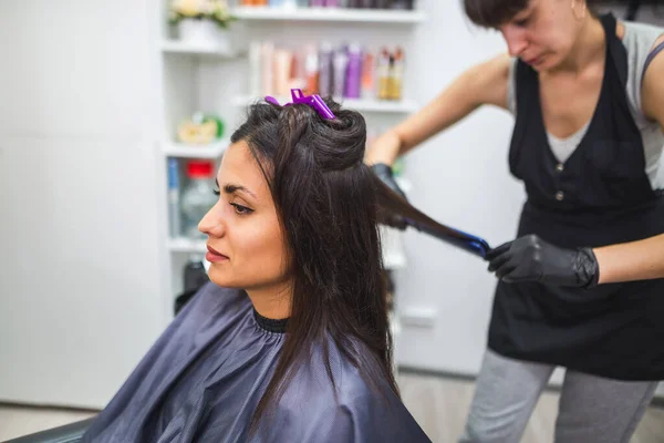 Hairdresser using a hair straightened to straighten the hair. Hair stylist working on a woman\'s hair style at salon.Hair care. Beautiful, attractive woman in a beauty salon.