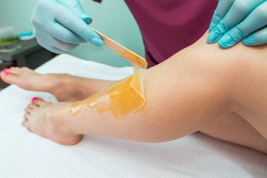 Woman undergoing leg hair removal procedure with sugaring paste in salon. Skin care, remove hair with sugar paste
