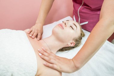 female masseuse massaging the shoulders and arms of a young woman lying on a couch with her eyes closed