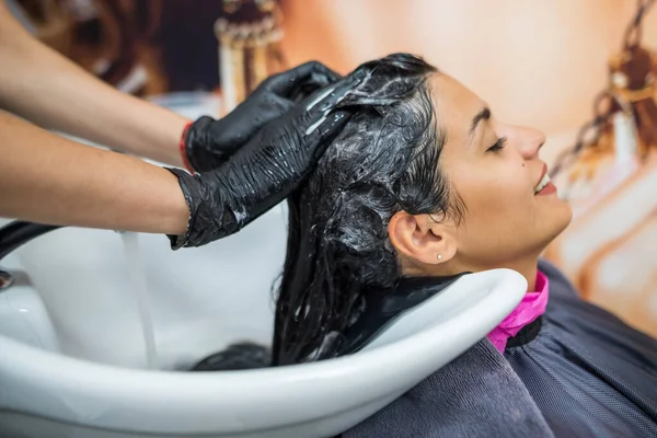 female client washes hair in salon, professional hairdresser washes head of female client with water and shampoo treatment, hairstyle beauty hair care, fashion service.