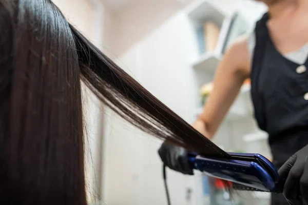 Hairdresser using a hair straightened to straighten the hair. Hair stylist working on a woman's hair style at salon.Hair care. Beautiful, attractive woman in a beauty salon.