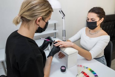The manicurist applies a base layer to the client's nail.Applying a transparent varnish with a brush.The alignment of the nail plate with nail Polish.Professional  manicure in a beauty salon.