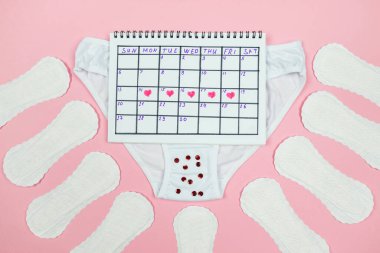 Top view photo of red heart marks on calendar, panty,sanitary pads on isolated pastel pink background