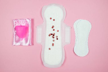 Top view photo of two panty liners and a pink menstrual cup on an isolated pastel pink background