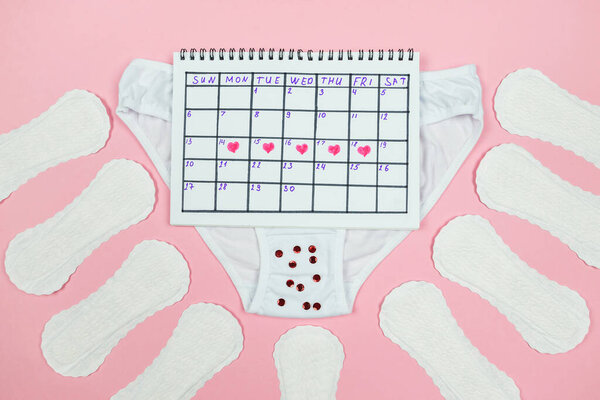 Фото красных отметок сердца в календаре, трусики, гигиенические прокладки на изолированном розовом фоне