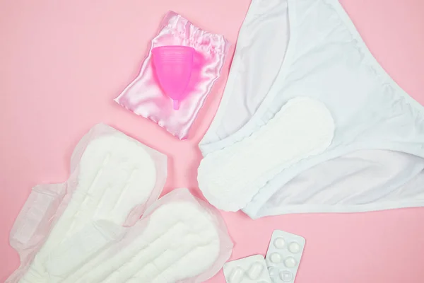 Top view photo of sanitary napkins, underwear, menstrual cup on isolated pastel pink background