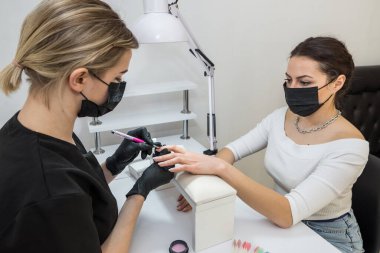 The manicurist applies a base layer to the client's nail.Applying a transparent varnish with a brush.The alignment of the nail plate with nail Polish.Professional  manicure in a beauty salon.